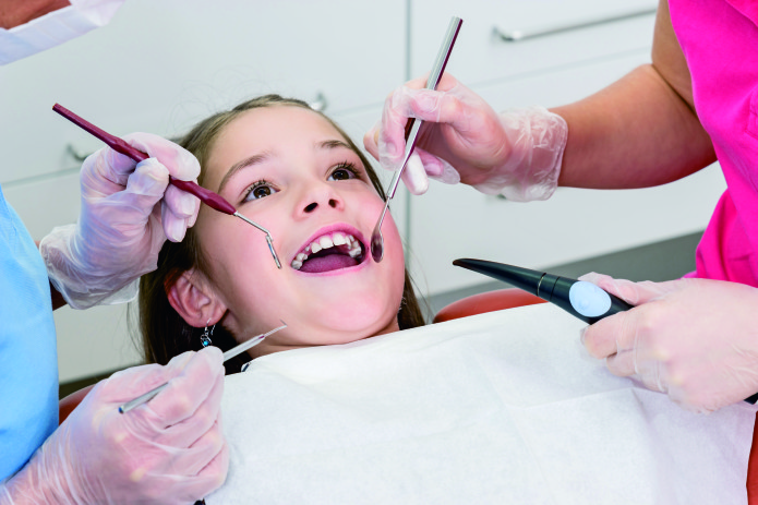 Mädchen liegt entspannt mit offenem Mund bei Zahnuntersuchung